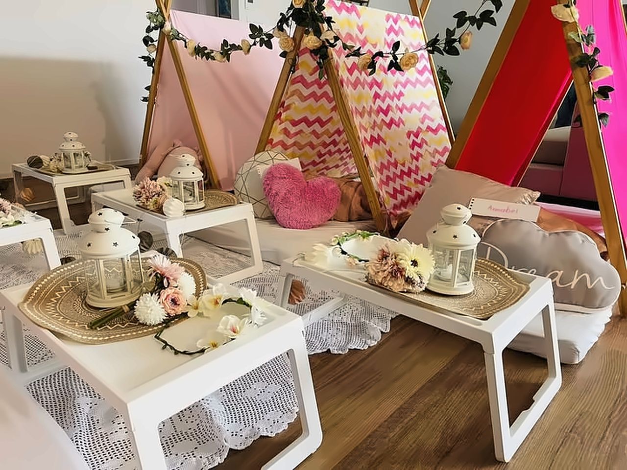 A styled boho teepee sleepover setup with flower cushions, lanterns and tray tables